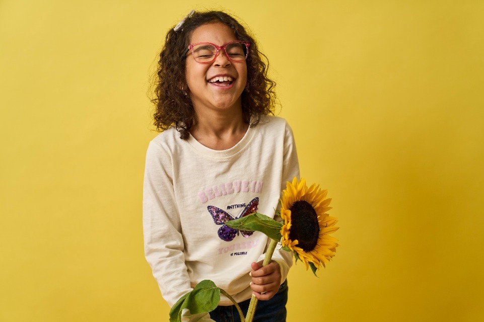 Ein Mädchen lachend mit einer Sonnenblume in der Hand